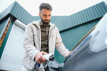 Portrait of a young man standing with charging cable near the charging station