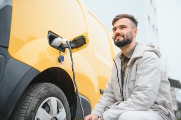 Casual man near electric car waiting for the finish of the battery charging process