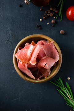 Italian cuisine prosciutto ham in a bowl on a dark table.