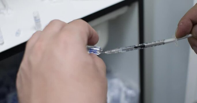 The doctor draws a dose of medicine for injection from a glass ampoule with a syringe. Preparation of a solution for subcutaneous injection with a syringe needle.