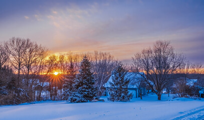 Tranquil view of Midwestern neighborhood at sunset in winter; snow on trees, buildings and the ground