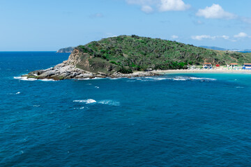 Vista de cima da praia das Conchas, próxima a cidade de Cabo Frio, com praias de areia branca, céu azul, mar com águas limpas e em tom de azul, com montanhas ao fundo.