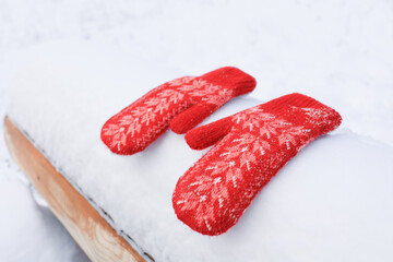 Red mittens lie on a snow-covered bench in a bright day. Selective focus.