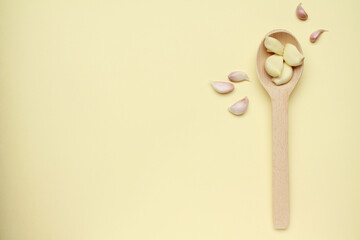 Fresh garlic cloves on wooden spoon on yellow color background. Vegan, organic, vitamins. Natural antibiotic, antioxidant, Allicin. Top view. Flat lay. Copy space for text