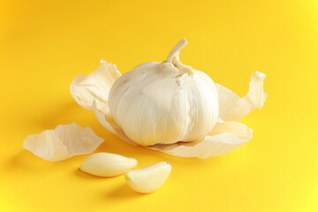 Fresh white unpeeled head bulb of garlic and garlic cloves peel on yellow color background. Vegan, organic, vitamins. Natural antibiotic, antioxidant, Allicin. 