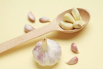 Fresh white unpeeled head bulb of garlic and garlic cloves on yellow color background with wooden spoon. Vegan, organic, vitamins. Natural antibiotic, antioxidant, Allicin. 