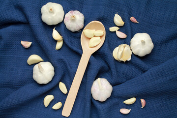 Fresh white unpeeled head bulb of garlic and garlic cloves on blue cloth fabric background with wooden spoon. Vegan, organic, vitamins. Natural antibiotic, antioxidant, Allicin. Top view. Flat lay