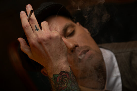 Relaxed man with closed eyes smoking in dark interior