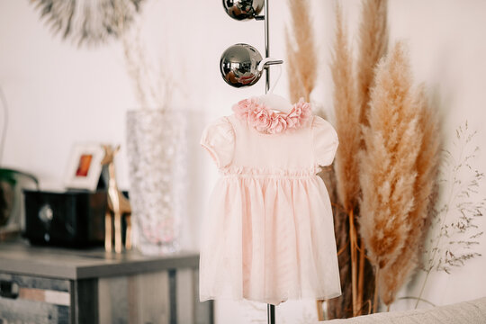 Little pink dress of baby for baptism ceremony for birthday party hanging in room