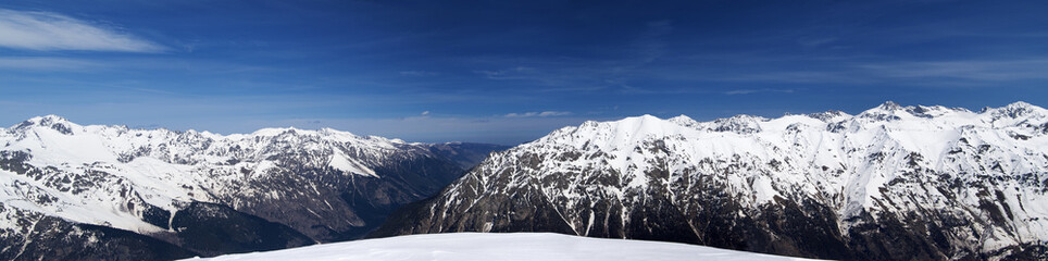 Panorama of high snow-capped mountain peaks and beautiful sky with clouds at sunny day.