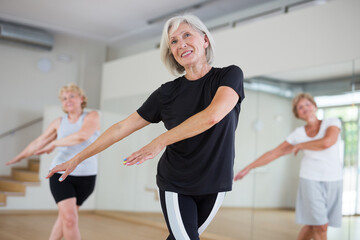 Active mature woman visiting choreography class with group of aged females, learning modern dynamic...