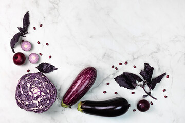 Purple color top view foods, red cabbage, eggplant, red onion, beans and basil on a marble background