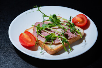 sandwich with bacon and microgreens and tomatoes on a black background