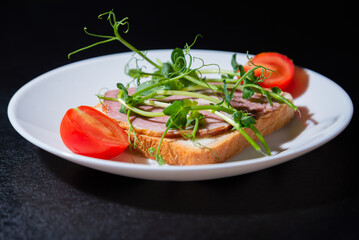 sandwich with bacon and microgreens and tomatoes on a black background