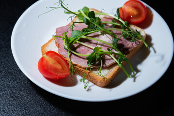sandwich with bacon and microgreens and tomatoes on a black background