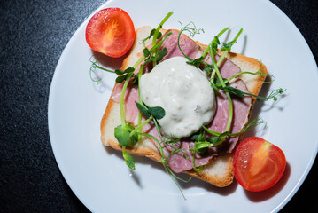 sandwich with bacon and microgreens and tomatoes on a black background