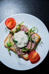 sandwich with bacon and microgreens and tomatoes on a black background