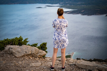 Girl standing on the rock above Zlatni Rat beach on the highest point of Brac island, the Vidova Gora mountain peak, taking photo of landscape