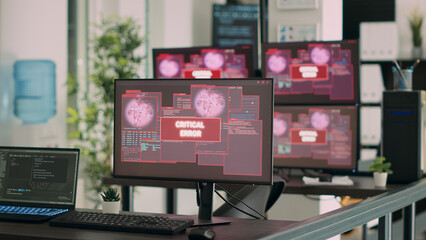 Empty it office desk with multiple computers showing security breach warning on network app. Monitors displaying critical error message flashing on screen with system crash alert.