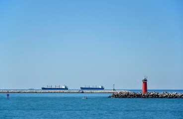 Cargo ships in blue sea and lighthouse on the pier