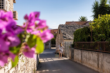 Girl walking in beautiful streets of Supetar, small town on Brac island, Croatia with stone houses and mediteranean vegetation, famous tourist destination