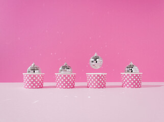 Disco ball in a paper cup with abstract cupcake flying one against a pastel pink background. Creative New Year or Xmas celebration party concept. Festive food idea. Creative art minimal aesthetics.