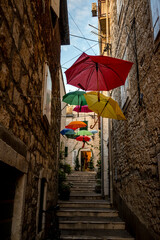 Fototapeta na wymiar Beautiful, old alley with suspended colorful umbrellas above the staircase in town of Milna, small town on Brac island, Croatia