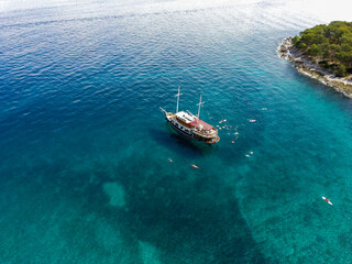 Aerial photo of tourist sailing boat anchored in magnificent, turquoise bay of Brac island, with people swimming in the crystal celar water