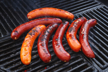 Traditionelle deutsche Bratwurst vom Grill angeboten als close-up auf einem Holzkohlegrill mit Feuer und Rauch 