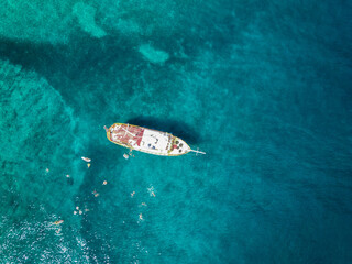Fototapeta na wymiar Aerial top down view of tourist ship anchored in the amazing, turquoise shallows of Brac island, Croatia with people swimming in the water