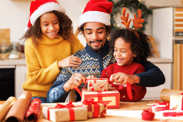 Happy ethnic family father and children pack Christmas gifts