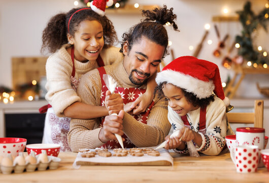 Happy ethnic family father and two kids in festive outfit making Christmas cookies together in kitchen