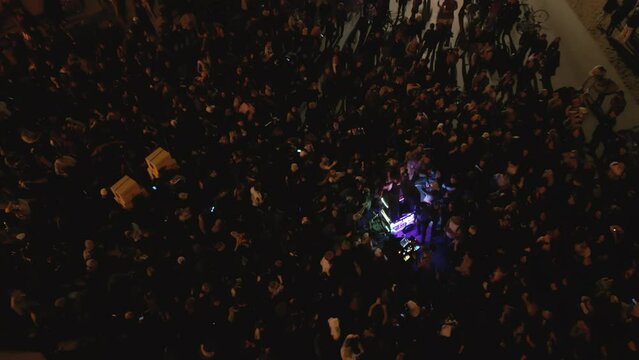 Aerial drone shot above crowd at open-air concert at night on the coast
