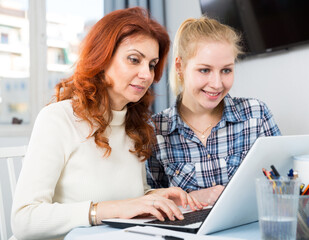 Portrait of mom and daughter at table using laptop together. High quality photo