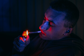 Portrait of a man in neon who smokes a joint. Guy smokes joint, marijuana, drugs cbd and thc.