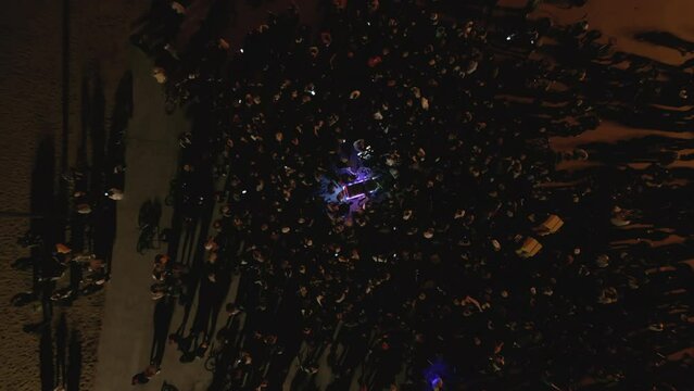 Aerial top shot of a crowd at open-air dnb dj set at night on the beach