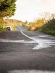 Small narrow asphalt road in a country side with a car parked off road. Selective focus. Travel and tourism concept.