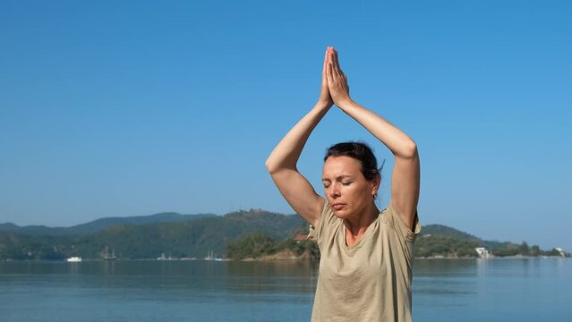Thoughtful woman with namaste hands. A woman rise her hands in namaste pose against blue sky. A concept of sea meditation and recreation time doing yoga.