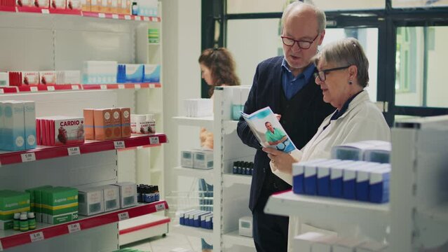 Health specialist reading pharmacy leaflet to elderly customer, talking about prescription medicine to cure disease. Pharmacist and male client looking at medicaments flier for support.