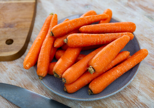 Image of a fresh whole carrot on a plate standing on a wooden table. Ingredients for cooking