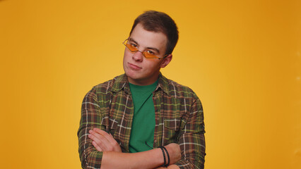 Playful happy teenager adult man 20 years old wearing yellow sunglasses blinking eye looking at camera with toothy smile, winking and flirting expressing optimism. Young guy boy on yellow background
