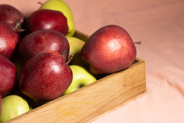 Wooden box with red and yellow apples on a pink background - close-up plan