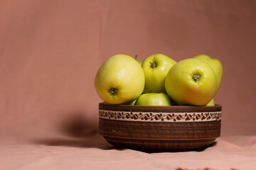 still life golden apples in a clay plate with a pattern on a pink background