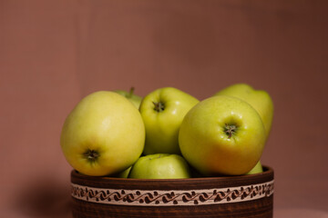 Delicious juicy golden apples on a background in a clay plate with an ornament with a blurred pink background