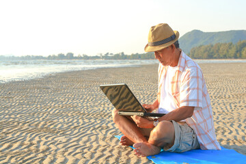 Asian elderly man Sit and work on the beach. Retirement tourism. Health insurance. Elderly society in retirement age.