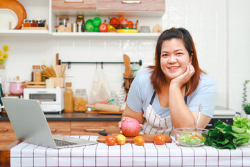Fat Asian woman enjoying cooking in the kitchen Learn to make salads and healthy meals from social media. Health care concept. Eat healthy food to lose weight.
