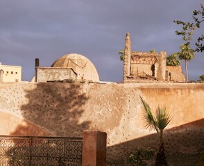 Stone wall with dome beyond, with dark, grainy sky and shadow of tree, Marrakech or Marrakesh, Morocco