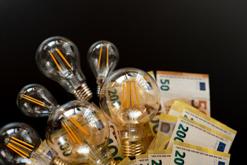Electricity cost.Light bulbs and euro banknotes on a black background. Rising electricity...