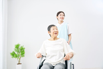 高齢者女性の乗る車椅子を押す介護士