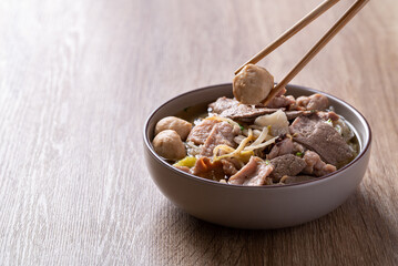 Rice noodles soup with pork in bowl eating by chopsticks on wooden background, Asian food
